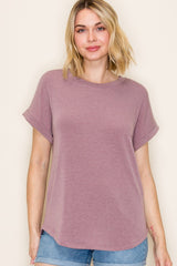 woman wearing a mauve short sleeve top with rolled cuffs and a relaxed fit, paired with denim shorts