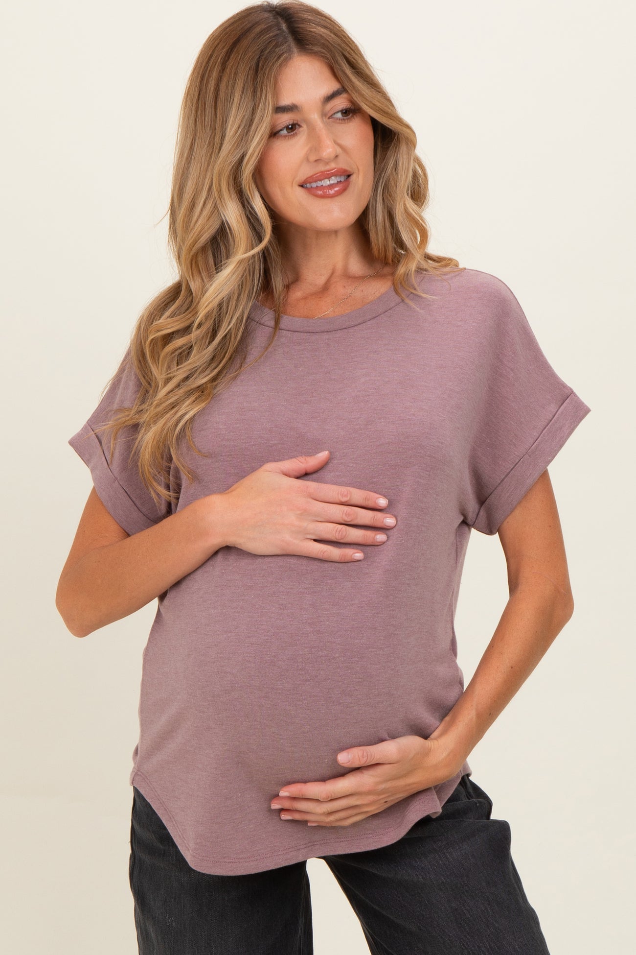 woman wearing a mauve short sleeve maternity top and holding her baby bump