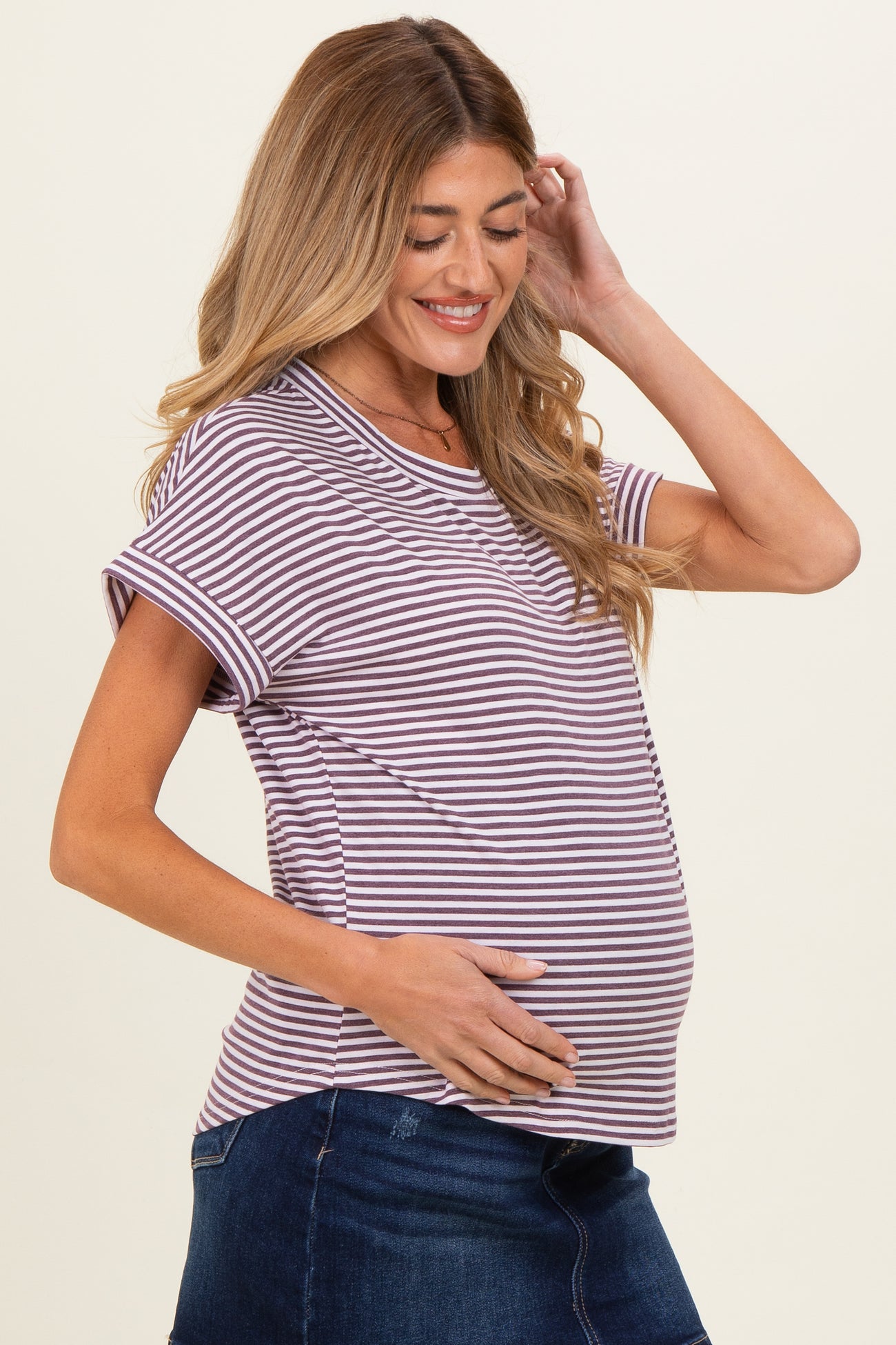 woman wearing a striped maternity top in shades of purple and white, holding her baby bump while smiling