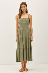 woman wearing an olive green smocked midi dress with adjustable straps and a tiered skirt