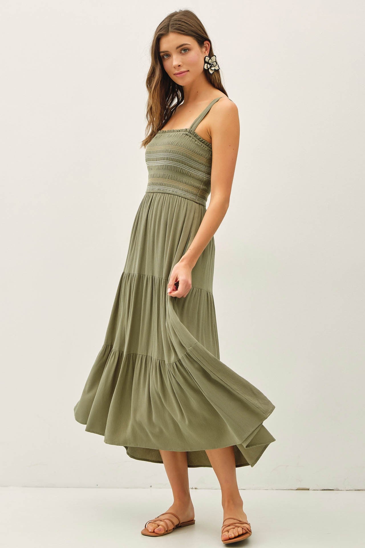 woman wearing an olive green smocked maxi dress with tiered skirt and thin straps, standing with one hand on her hip
