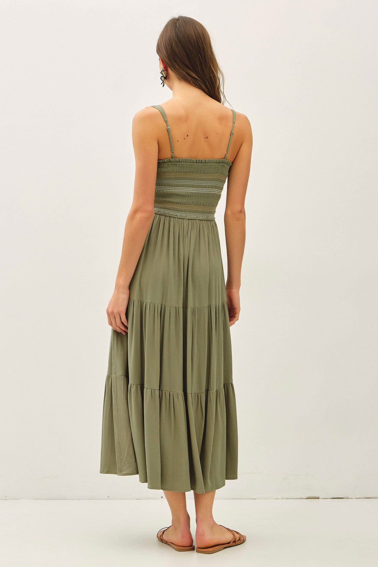 woman wearing an olive green tiered maxi dress with a smocked bodice and thin straps seen from the back