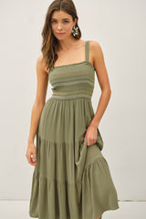 woman wearing a sage green smocked midi dress with a tiered skirt and wide straps