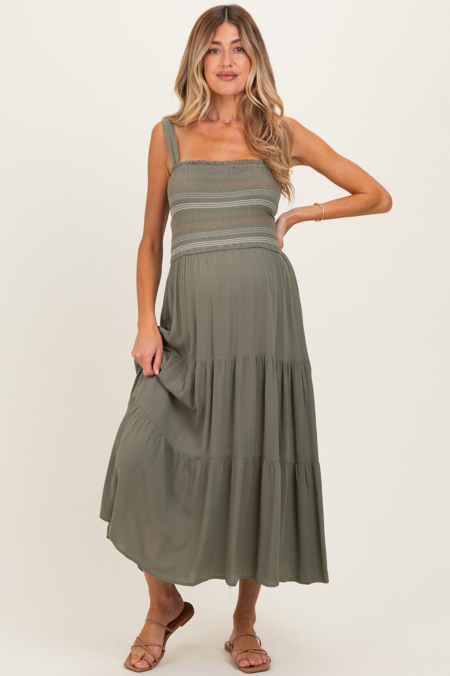 woman wearing a sage green maternity maxi dress with smocked top and tiered skirt, holding her baby bump