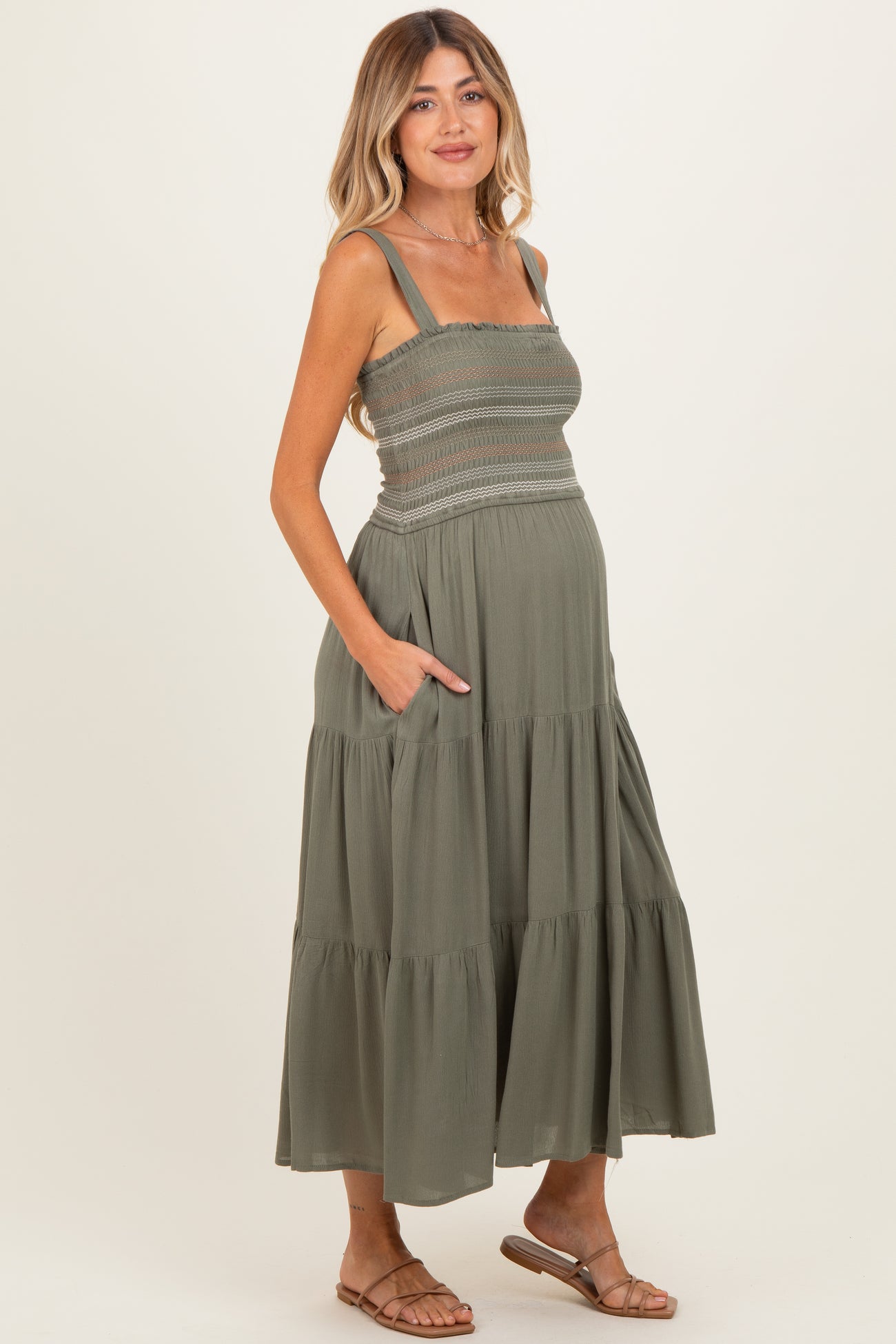 woman wearing a dark green maternity maxi dress with smocked bodice and pockets, showing her baby bump