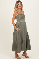 woman wearing a dark green maternity maxi dress with smocked bodice and pockets, showing her baby bump