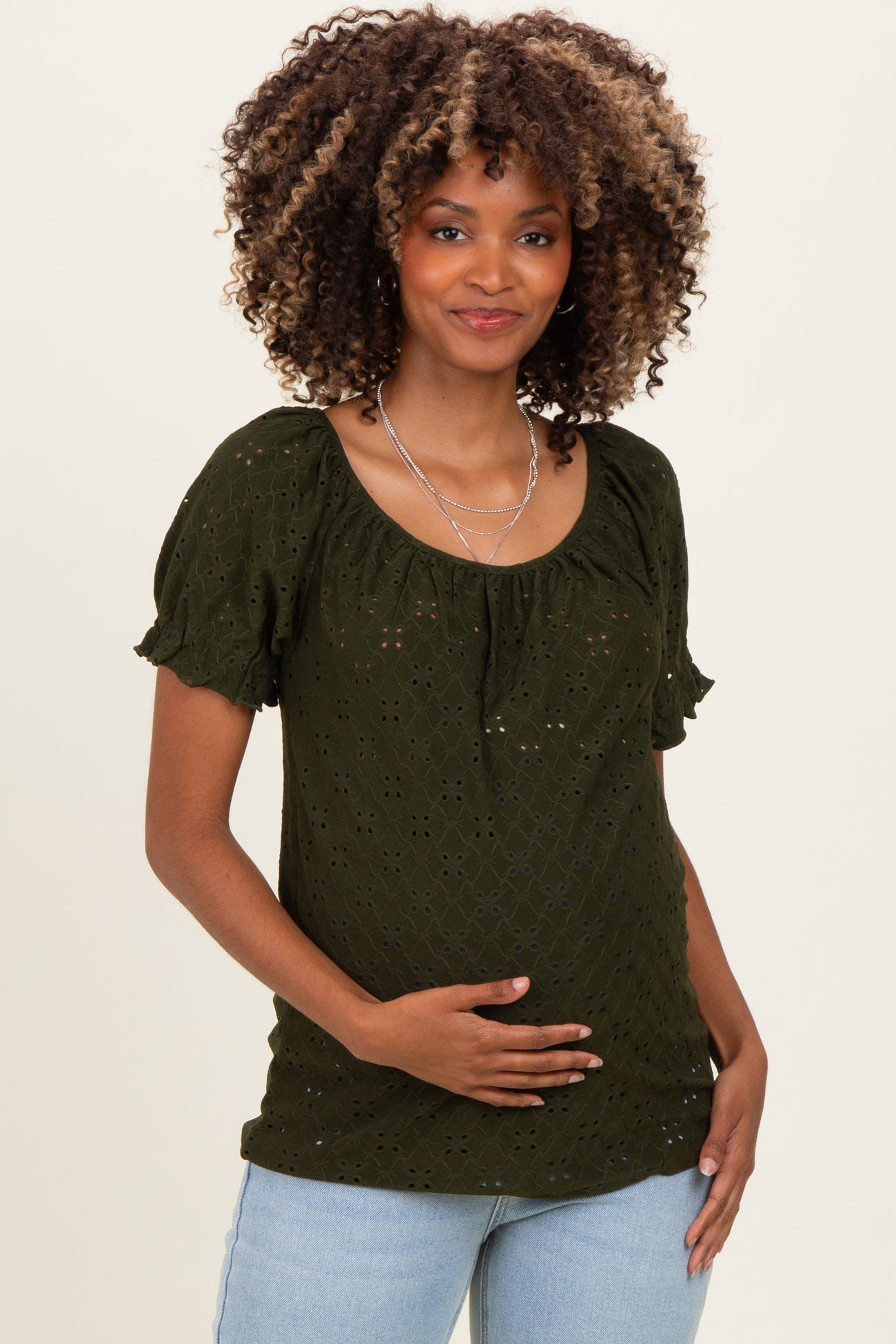 woman wearing a dark green maternity top with short puff sleeves, holding her baby bump