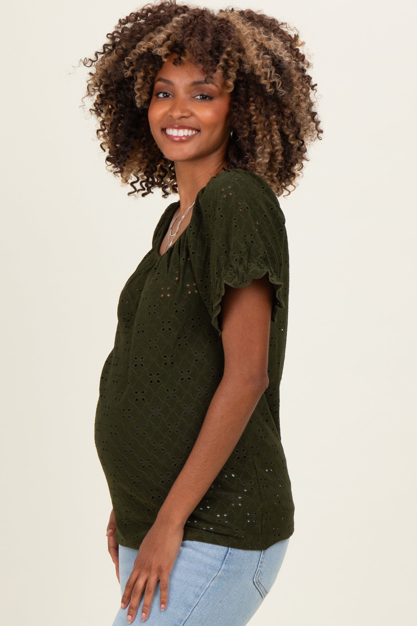 woman wearing a dark green short sleeve maternity top with eyelet detailing and a visible baby bump