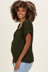 woman wearing a dark green short sleeve maternity top with eyelet detailing and a visible baby bump
