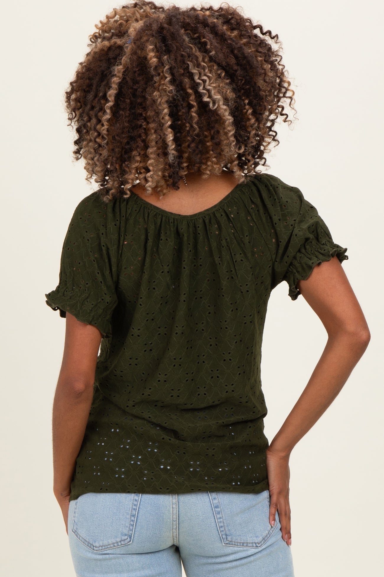 woman wearing a dark green short sleeve maternity top with a gathered neckline and lace details, showing her back