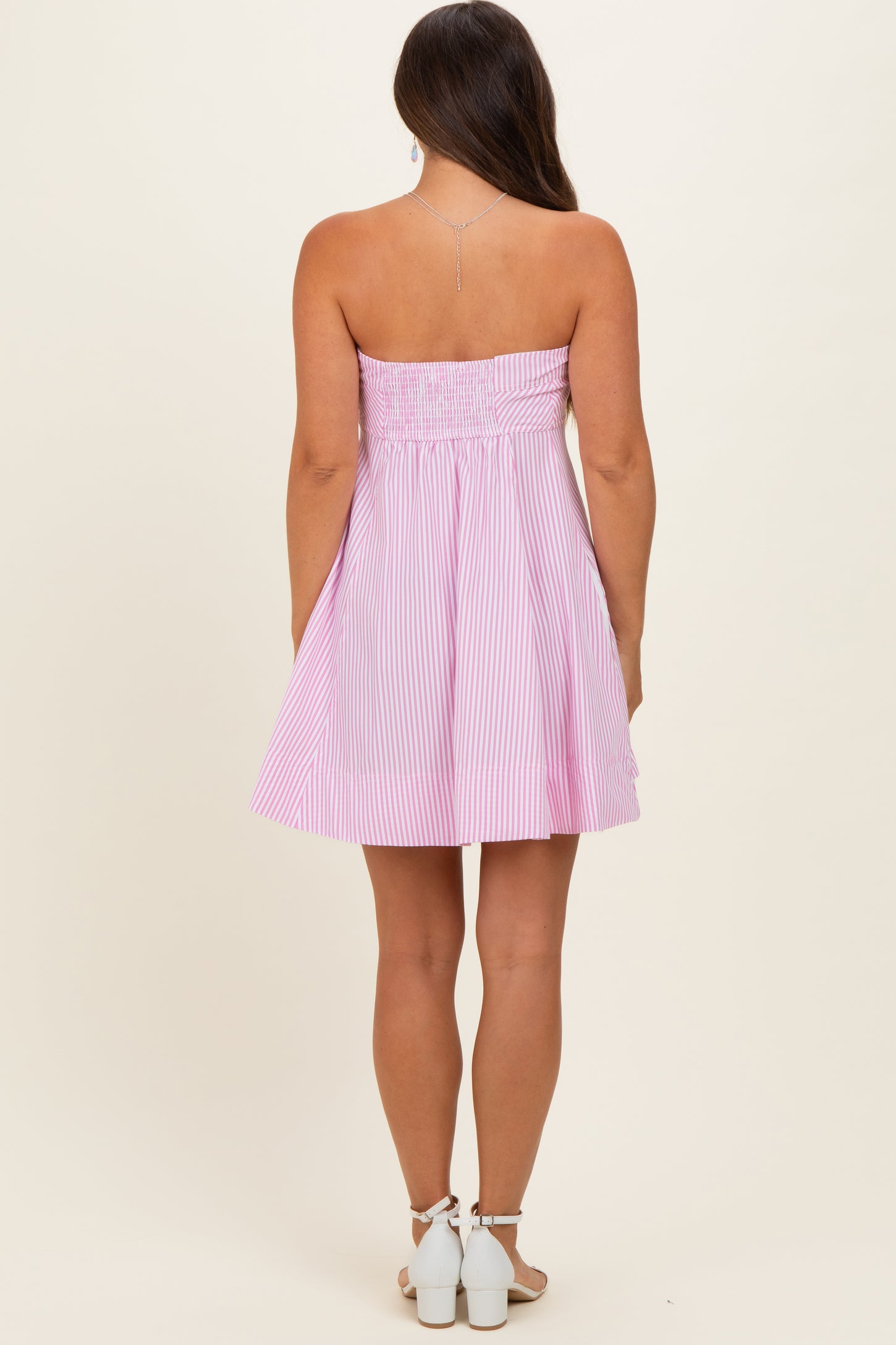 woman wearing a pink and white striped strapless maternity dress with a smocked bodice and flared skirt