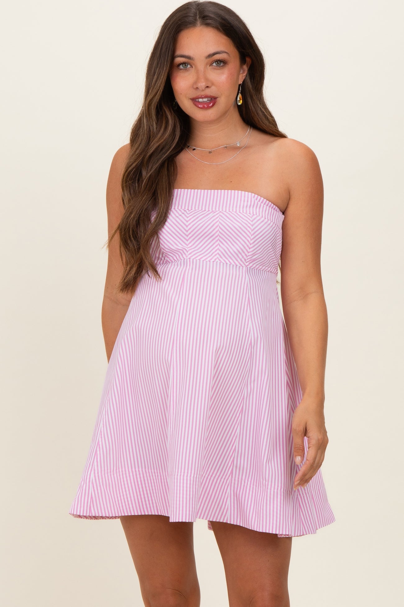 woman wearing a pink and white striped strapless maternity dress with a fitted bodice and flared skirt, showing her baby bump