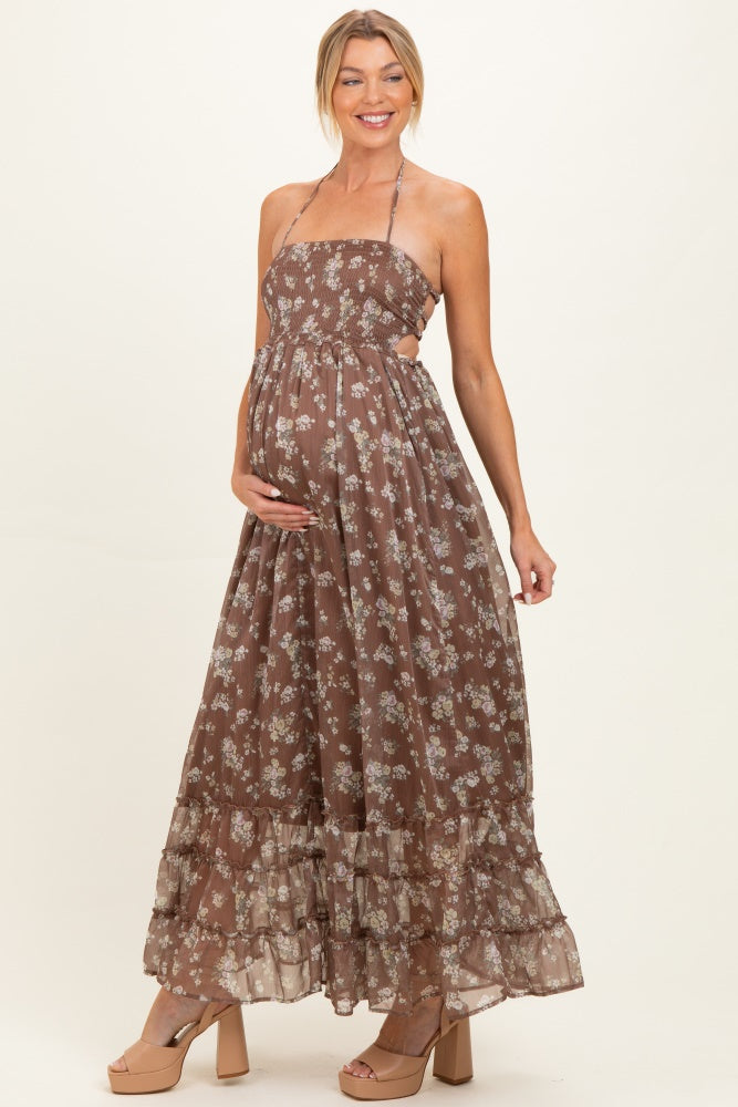 woman wearing a brown floral print maternity maxi dress with a halter neck and cut-out details, showcasing her baby bump