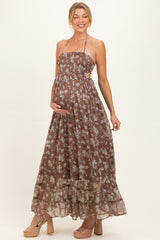 woman wearing a brown floral print maternity maxi dress with a halter neck and cut-out details, showcasing her baby bump
