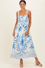 woman wearing a white maxi dress with blue floral print and scalloped hem, standing against a neutral background