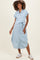 woman wearing a light blue striped maternity dress with a tie belt and short sleeves, standing and smiling