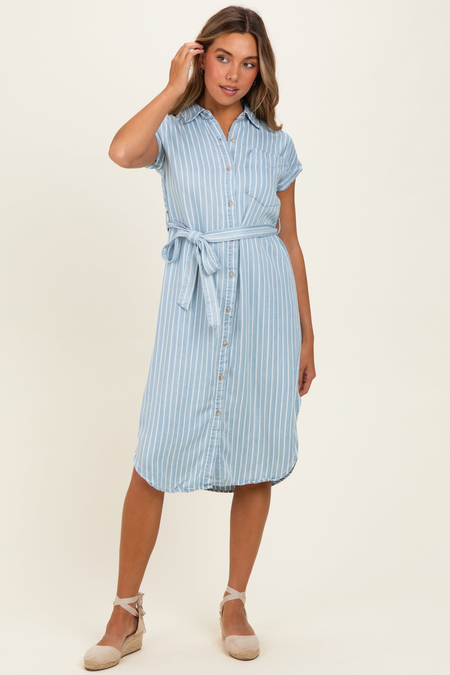 woman wearing a light blue striped button-up dress with short sleeves and a tie belt