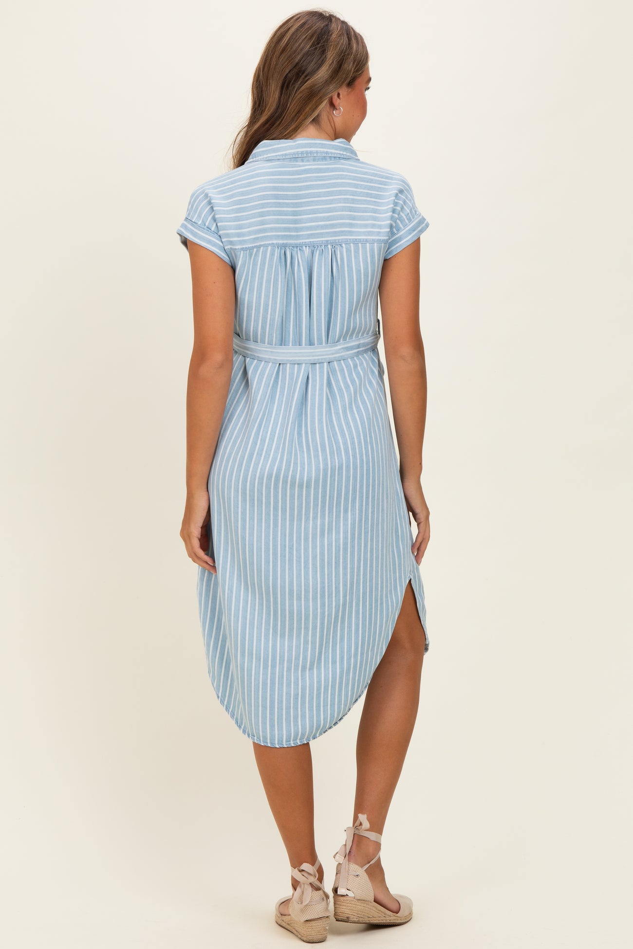 woman wearing a light blue striped shirt dress with a tied waist and rolled sleeves, viewed from the back