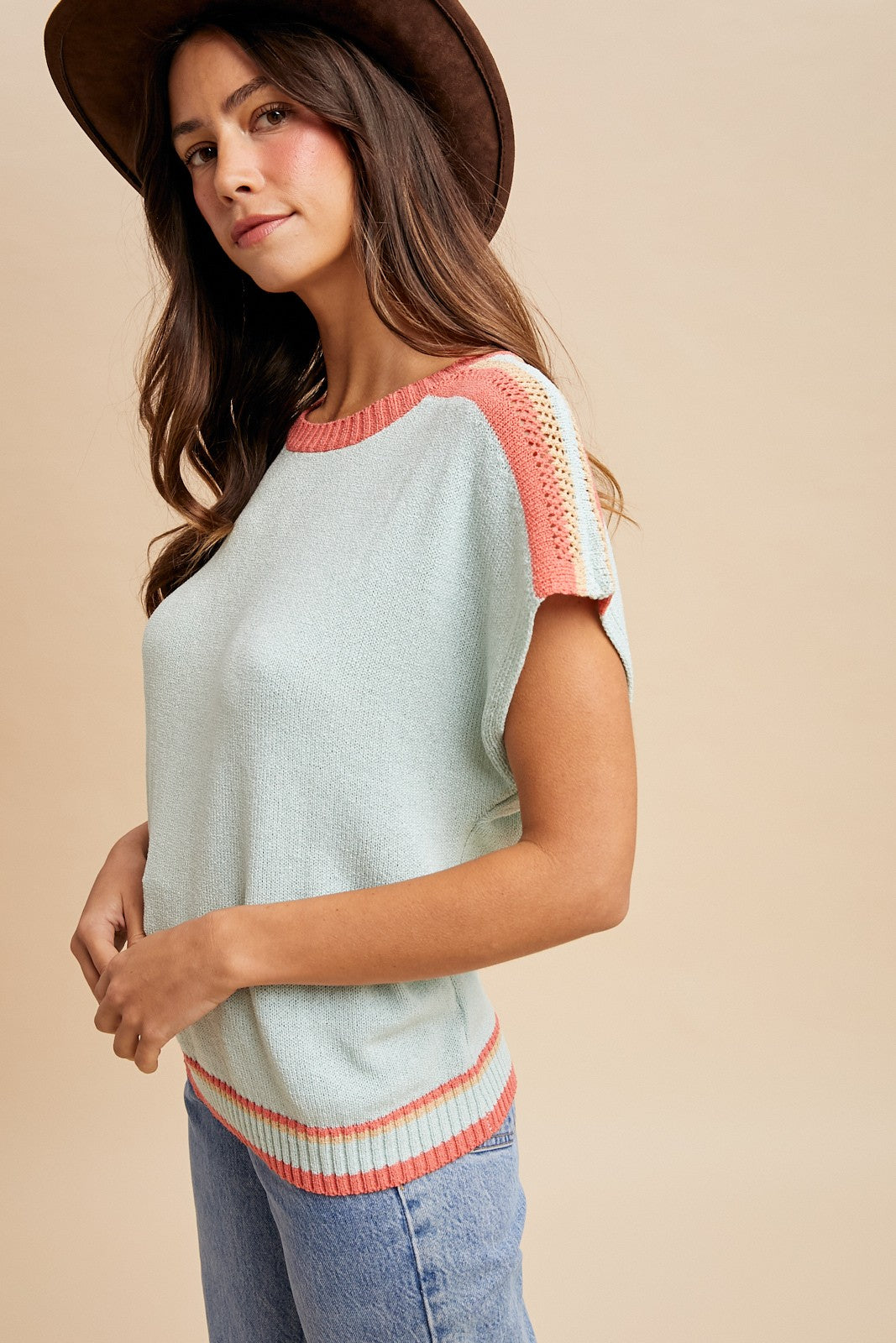woman wearing a light blue short sleeve sweater with coral accents and wearing a brown hat