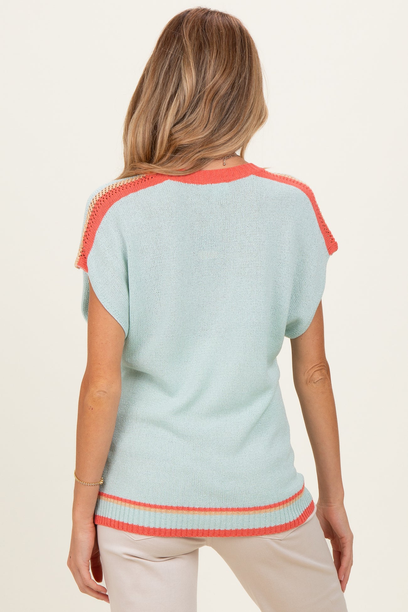 woman wearing a light blue maternity sweater with coral trim and short sleeves, viewed from the back