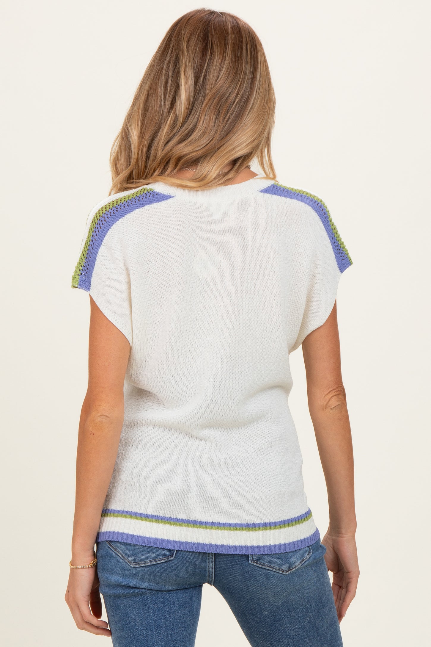 woman wearing a white maternity sweater with multicolored trim, showing the back while standing against a neutral background
