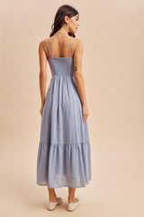 woman wearing a light blue maxi dress with adjustable spaghetti straps and a smocked bodice, standing with her back to the camera