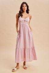 woman wearing a light pink maxi dress with adjustable straps, lace detailing, and pockets
