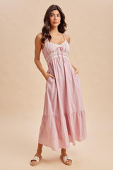 woman wearing a light pink maxi dress with lace detail and pockets, standing against a neutral background