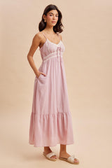 woman wearing a light pink maxi dress with lace detailing and pockets, styled with flat sandals