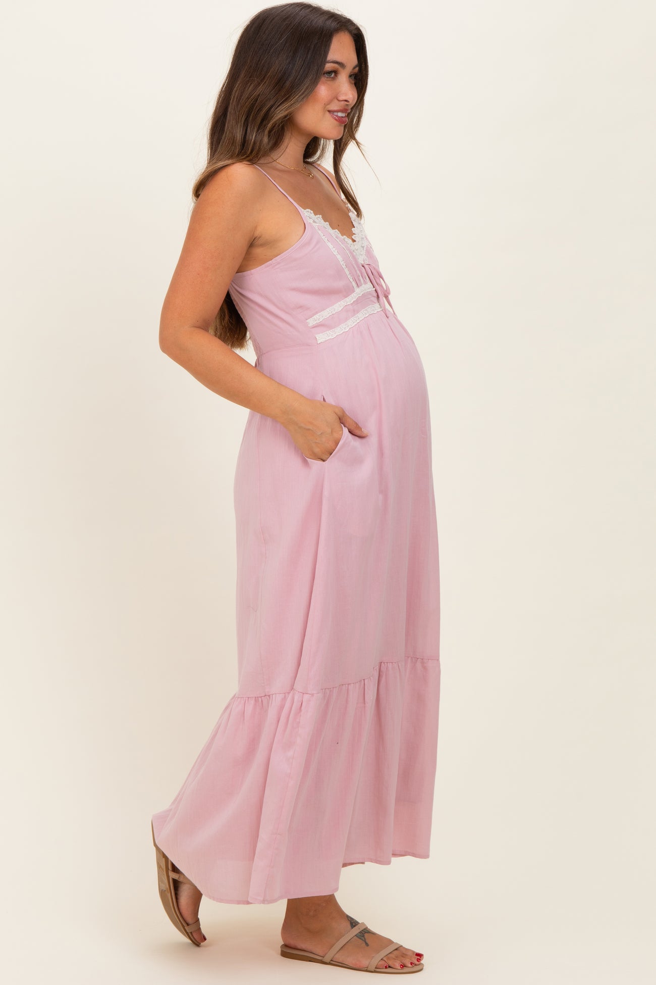 woman wearing a pink maternity maxi dress with lace details and pockets, showcasing her baby bump