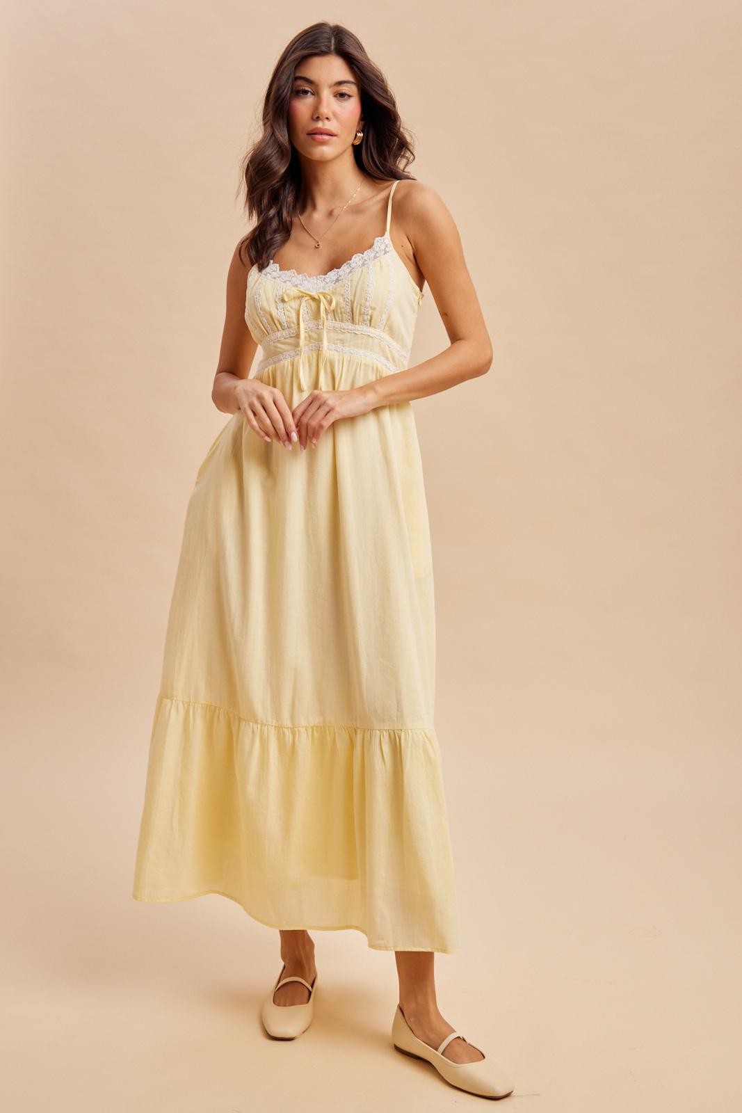 woman wearing a yellow maxi dress with lace detailing and a tiered skirt, standing against a neutral background