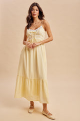 woman wearing a yellow maxi dress with lace detailing and a tiered skirt, standing against a neutral background