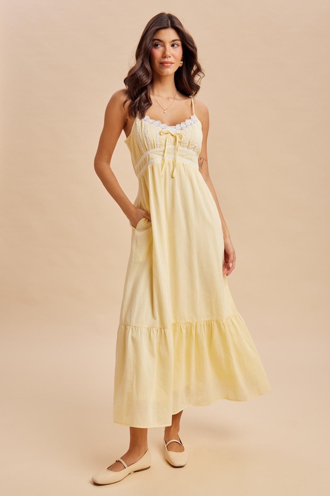 woman wearing a yellow maxi dress with lace detail and pockets, standing against a neutral background