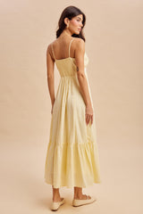 woman wearing a yellow maxi dress with a smocked bodice and tiered skirt, styled with simple slip-on shoes