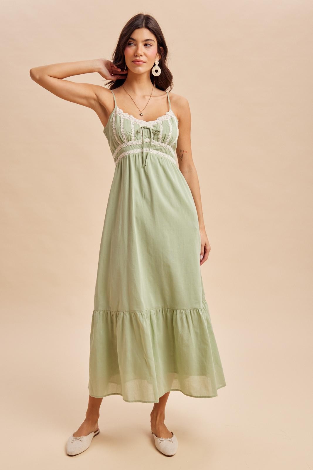 woman wearing a light green maxi dress with lace detailing and a tiered skirt, styled with flats and accessories