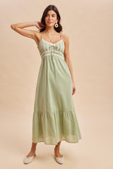 woman wearing a light green maxi dress with lace detailing and a tiered skirt, styled with flats and accessories