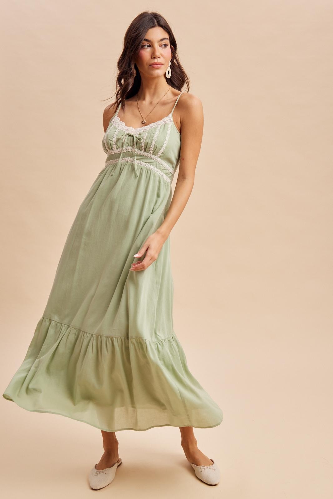 woman wearing a light green maxi dress with spaghetti straps and lace detailing, standing against a neutral background