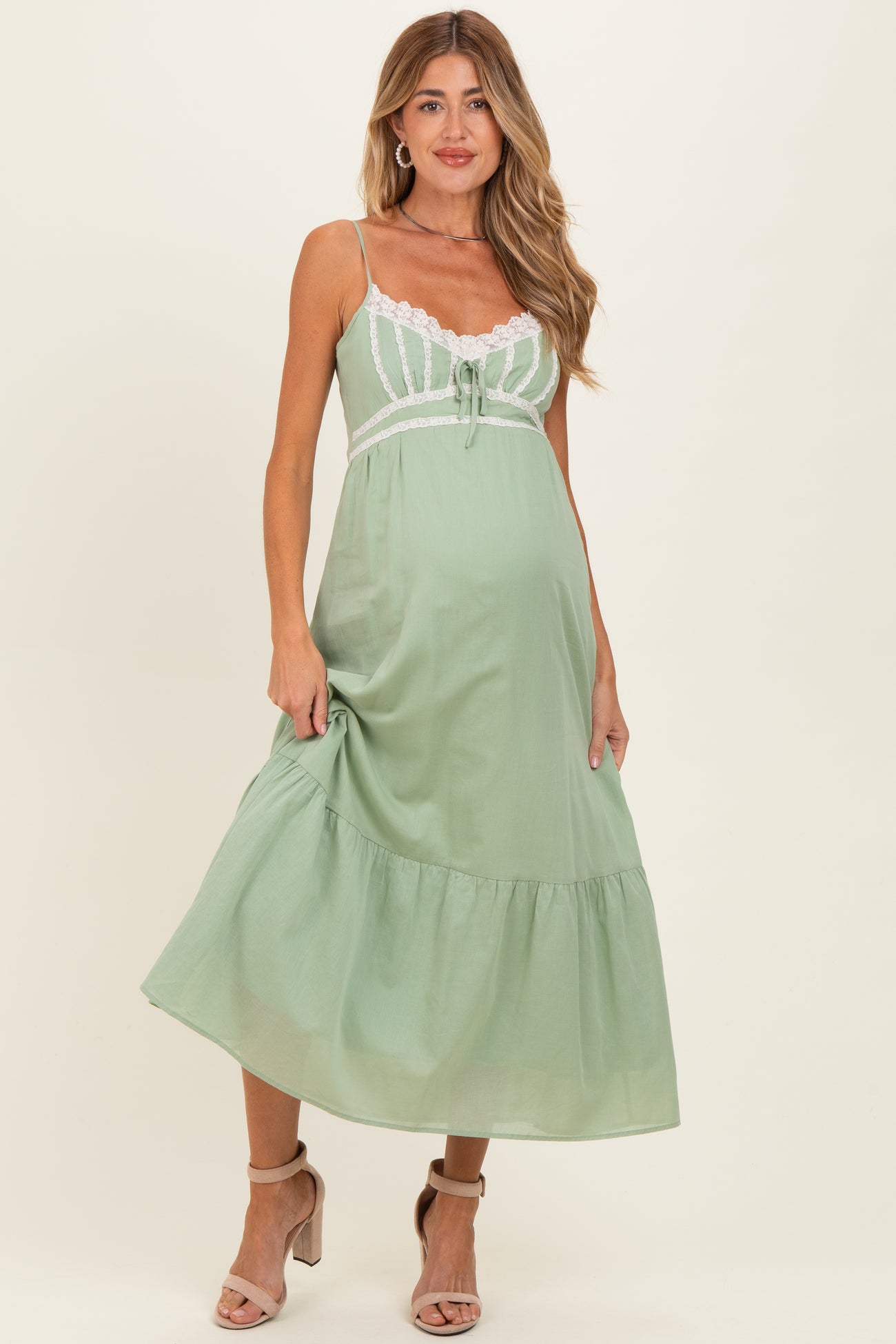 woman wearing a light green maternity dress with lace accents and a tiered skirt, showcasing her baby bump