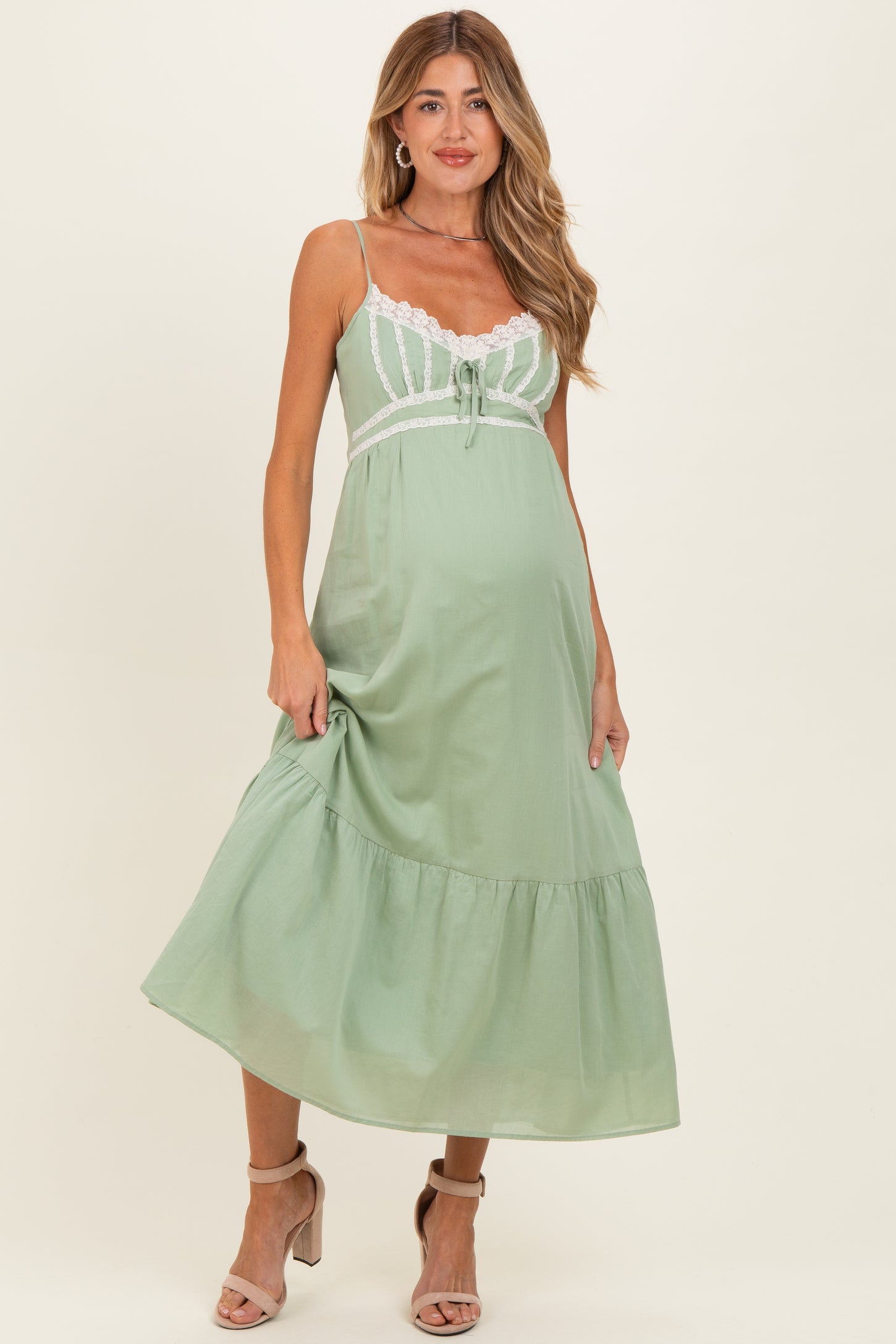 woman wearing a light green maternity dress with lace accents and a tiered skirt, showcasing her baby bump