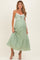 woman wearing a light green maternity dress with lace accents and a tiered skirt, showcasing her baby bump