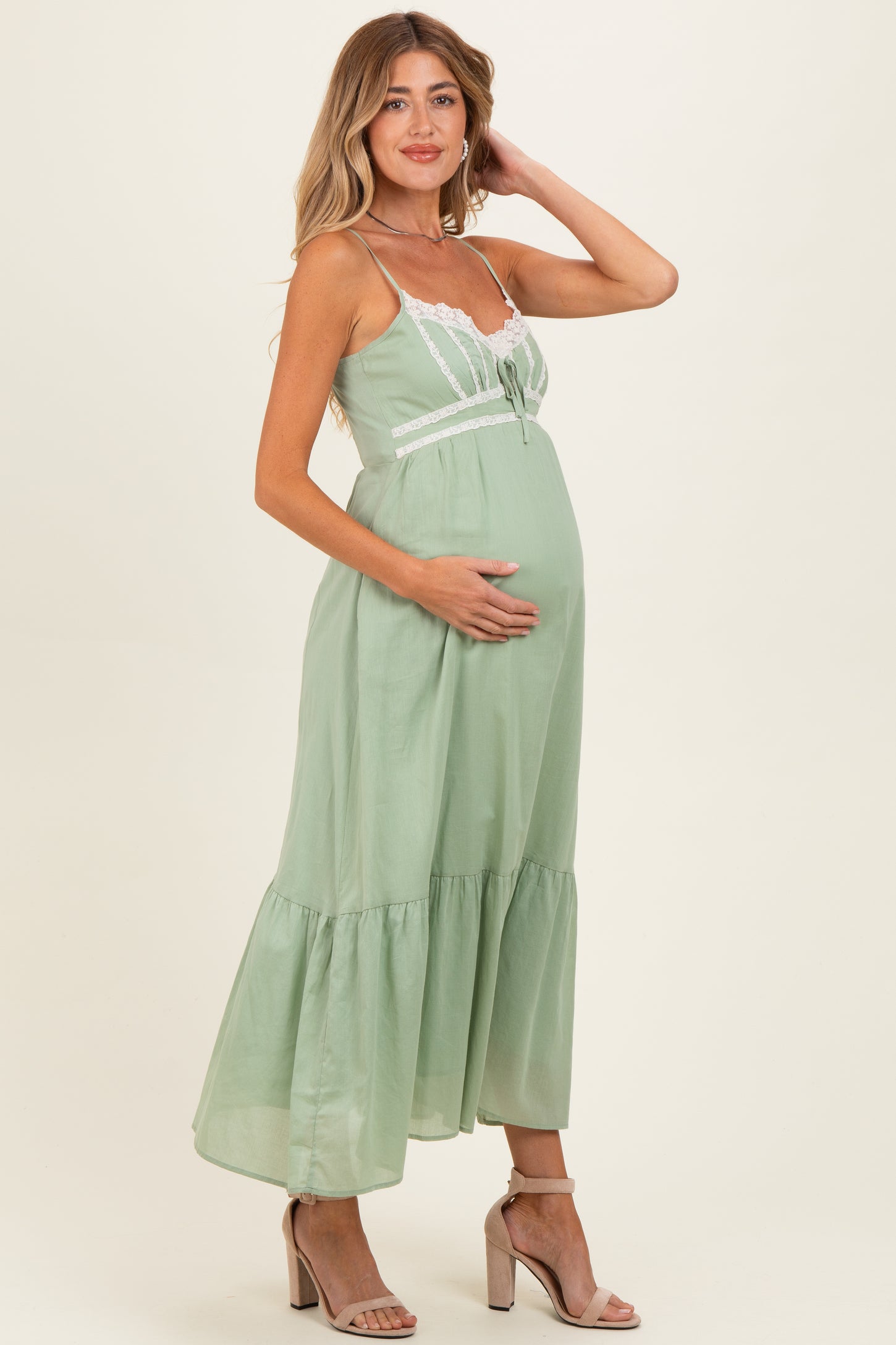 woman wearing a light green maternity maxi dress with lace details and holding her baby bump