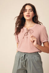 woman wearing a light pink short sleeve top with lace-up detailing and gray drawstring trousers