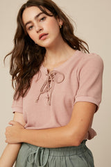woman wearing a light pink short sleeve top with a lace-up neckline and rolled cuffs