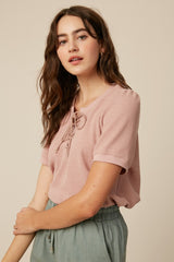 woman wearing a pink short sleeve top with a lace-up front detail and styled with light green pants