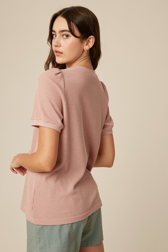 woman wearing a light pink puff sleeve top and green shorts, showing the back view of the top
