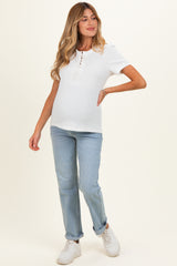 woman wearing a white short sleeve maternity top with lace-up detail and blue maternity jeans, showing her baby bump
