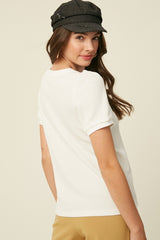 woman wearing a white short sleeve top with puffed sleeves and a black cap, viewed from the back