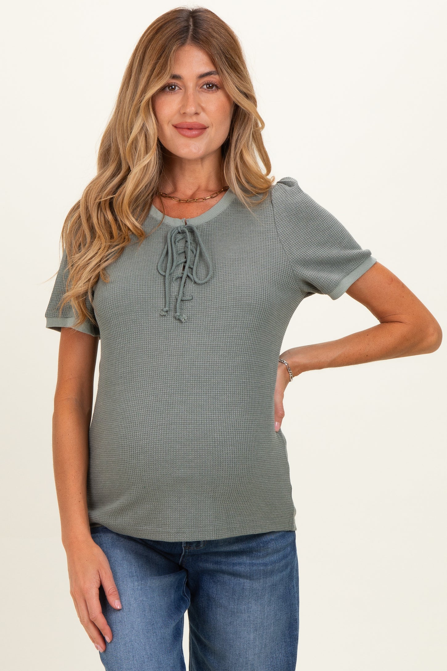 woman wearing a sage green short sleeve maternity top with lace-up front detail and a visible baby bump