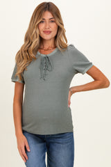 woman wearing a sage green short sleeve maternity top with lace-up front detail and a visible baby bump