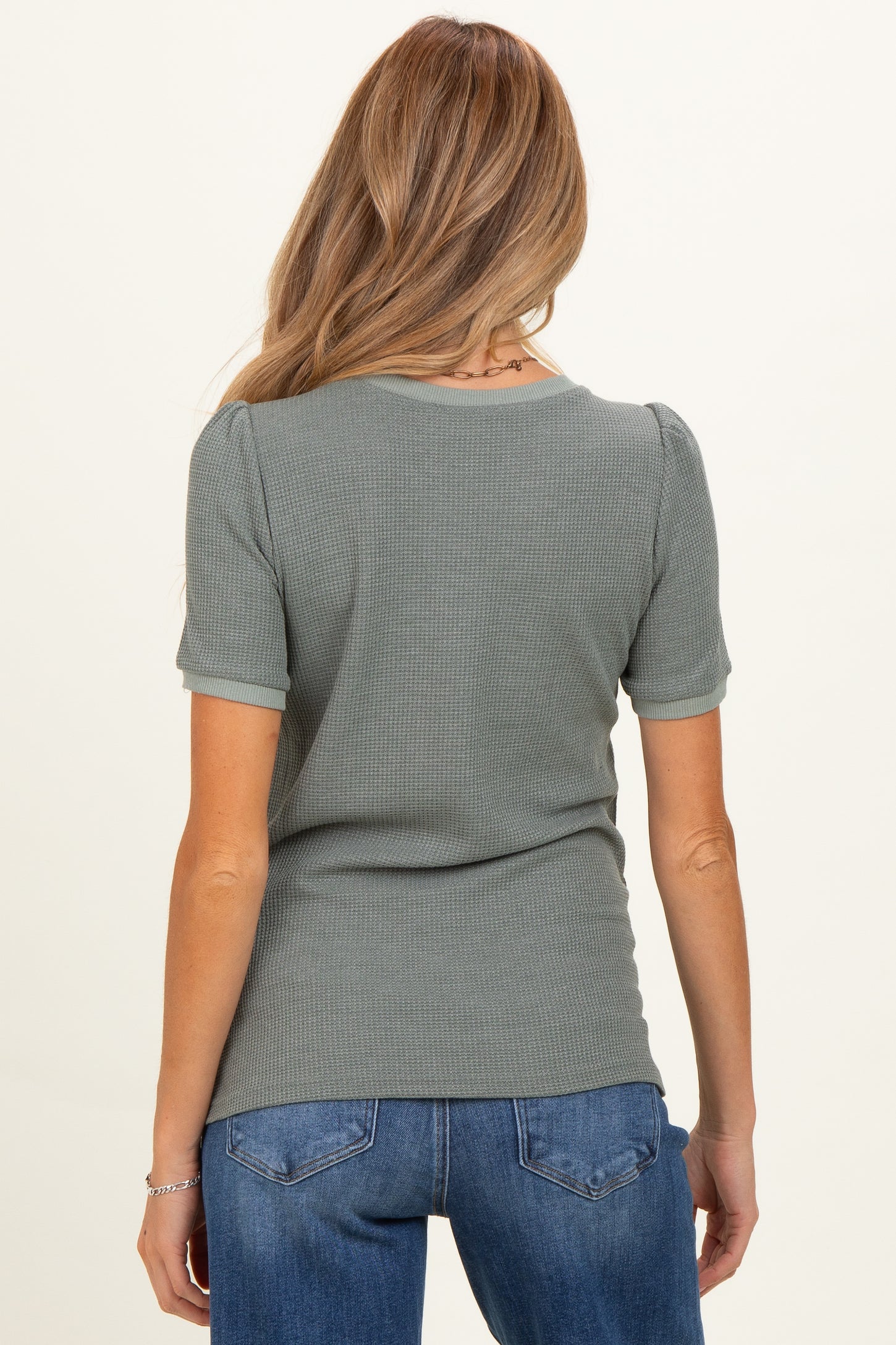 woman wearing a light green short sleeve maternity top with puffed sleeves viewed from the back